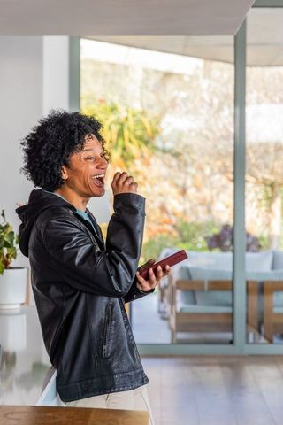 African american man laughing while leaning at home counter holding red smartphone