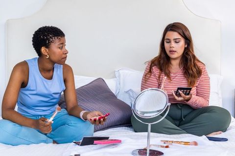 African american friends applying makeup on bed sharing beauty tips and laughter