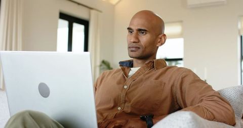 Mature african american man working on laptop checking smartwatch, calm focused remote worker