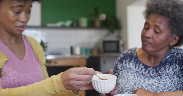 This image shows a younger woman preparing tea for an elderly woman in a kitchen. It is suitable for illustrating articles on family care, family dynamics, caregiving, or morning routines. The image brings an intimate, caring atmosphere that fits well with healthcare, lifestyle, and family-themed content.