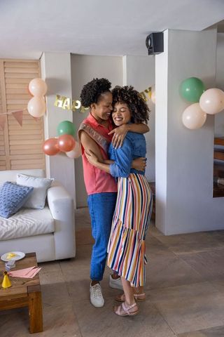 Two women hugging at home party with balloons and happy banner celebrating friendship