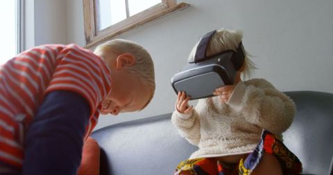 Young Siblings Using Virtual Reality Headset on Sofa at Home