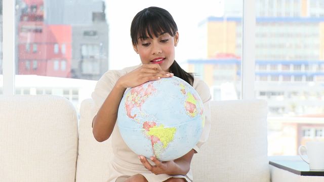 Young businesswoman intensely studying a terrestrial globe. Capture evokes themes of global strategy, international business planning, and reflection. Ideal for articles on global markets, business strategies, educational materials, or travel campaigns.