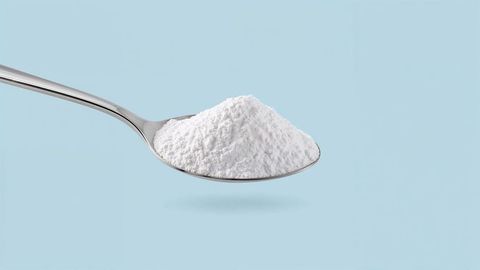 Stainless steel spoon with fine white milk powder against blue backdrop