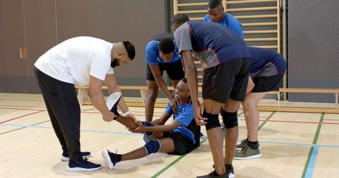 Volleyball player receiving help from teammates after ankle injury during indoor training