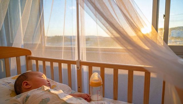 Sleeping baby basking in golden sunlight in wooden crib with feeding bottle