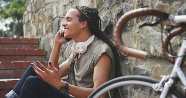 Fashionable biracial man with dreadlocks sitting on stairs and talking on smartphone. Street style, modern urban lifestyle and communication.