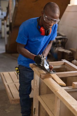 African american carpenter smoothing wood with hand plane in carpentry workshop