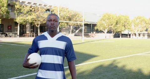 Young Athlete Holding Rugby Ball on Sports Field with Goalpost Background