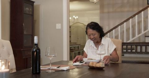 Asian senior woman dining alone in elegant home interior