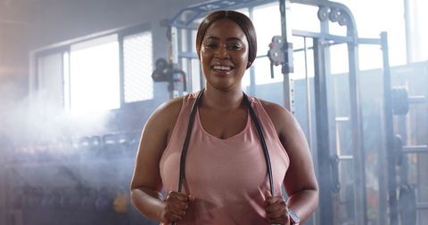 Mid-adult african american woman smiling holding jump rope in gym wearing pink tank top