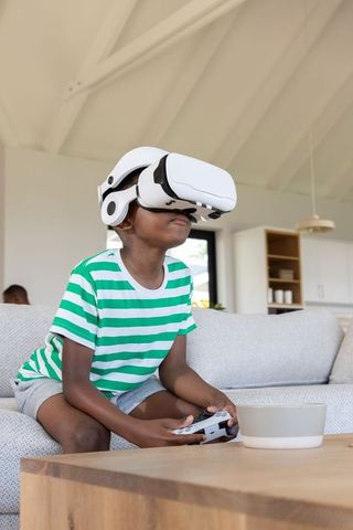 African american boy wearing vr headset with controller playing immersive game in living room