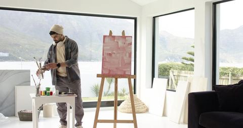 Indian painter creating abstract canvas in bright lakeside studio with mountain view