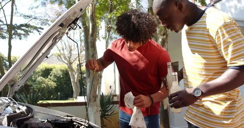 Male friends checking car oil level together outdoors