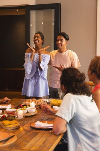 Friends celebrating at cozy dinner party — woman standing, guests toasting with charcuterie and cham