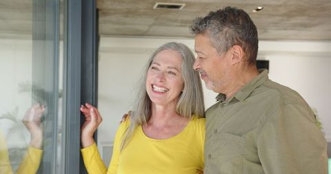 Senior Couple Smiling by Glass Door in Modern Home