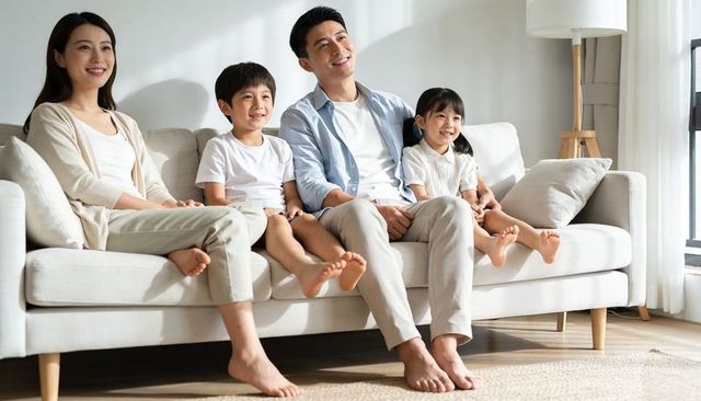 Smiling family relaxing on sofa in sunlit modern living room wearing casual clothes