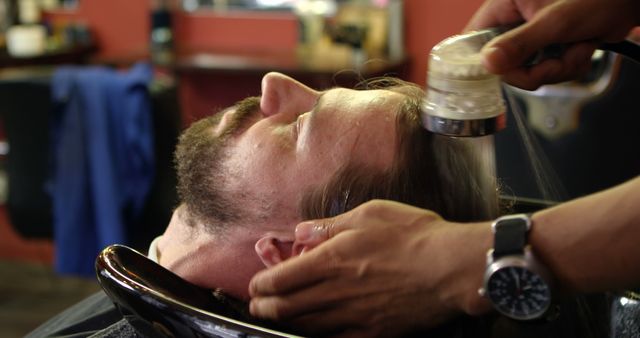 Male client getting his hair washed at a barbershop. Ideal for content on men's grooming, haircare routines, salon services, or professional barbering techniques.