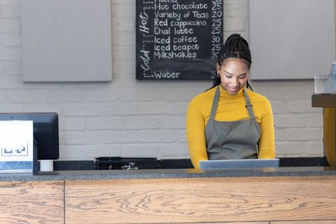 African american barista using tablet at wood counter in minimalist cafe with chalkboard menu