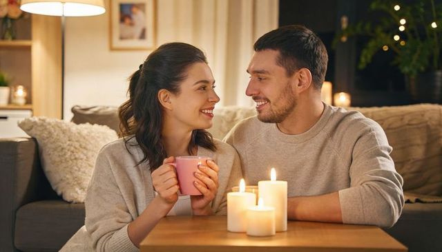 Romantic couple enjoying cozy candlelit evening on sofa with warm knit sweaters and mug