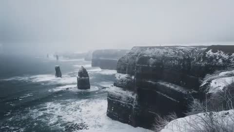 Panning across snowy coastal cliffs and sea stacks in moody winter ocean storm footage