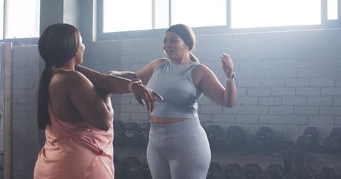 Diverse women stretching and motivating each other in sunlit gym studio during workout
