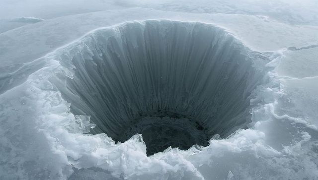 Revealing deep circular ice chasm on frozen lake with jagged rim and steep-walled shaft