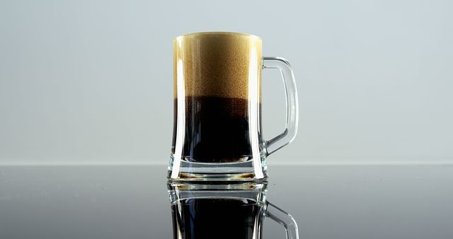 A clear glass mug filled with dark liquid, coffee, is showcased against a light background, with copy space. Its reflection on the glossy surface adds to the minimalist aesthetic of the composition.