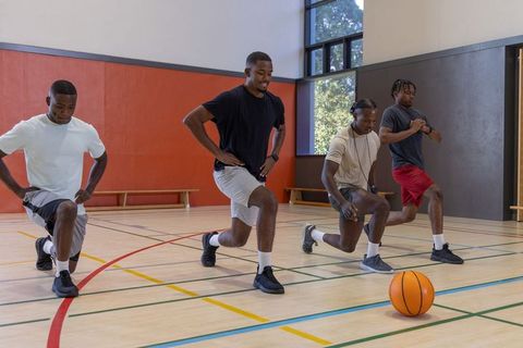 African american men doing lunges on basketball court for team conditioning