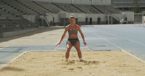 Caucasian female athlete long jumping on sand track