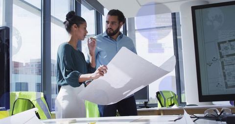 Architects reviewing large blueprint in sunlit modern office collaborating on urban design