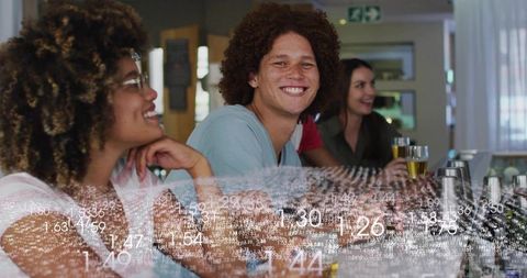 Smiling young man leaning on bar counter with friends enjoying pub drinks and conversation