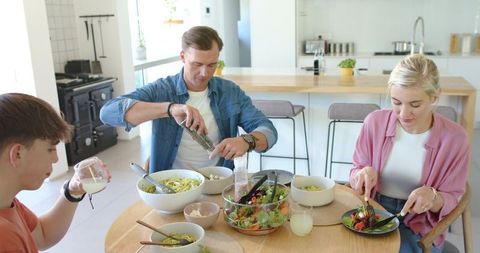 Family enjoying casual home-cooked dinner in bright modern kitchen, father seasoning pasta