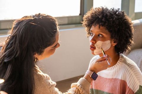 Diverse women applying white facial mask with brush sunlit home skincare ritual