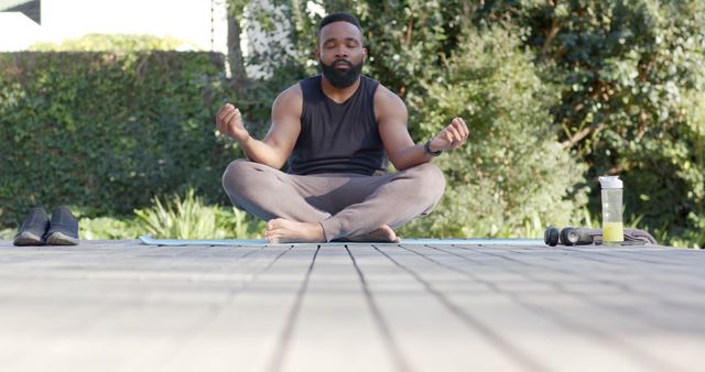 Man sitting cross-legged and meditating in a serene garden environment. Ideal for promoting mental peace, healthy lifestyle, and outdoor fitness activities. Suitable for wellness blogs, fitness websites, and health-related materials.