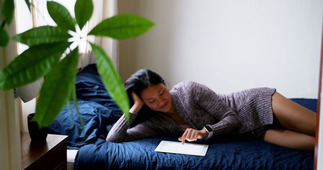 Woman using digital tablet while relaxing on bed in bedroom