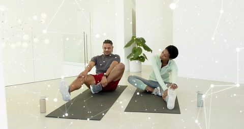 Friends stretching on yoga mats in minimalist fitness studio with plant and water bottles