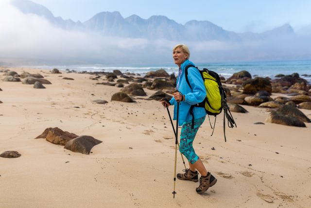 Caucasian hiker senior woman with backpack and hiking poles walking on the beach. trekking hiking and adventure concept.