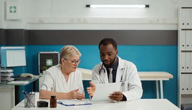 Senior woman consulting with physician reviewing medical records and treatment plan