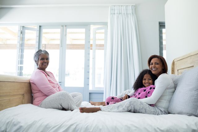This image shows three generations of women sitting on a bed, smiling and enjoying each other's company. It is perfect for use in advertisements, blogs, or articles about family bonding, multigenerational living, or home life. It can also be used in campaigns promoting family values, togetherness, and the importance of spending quality time with loved ones.
