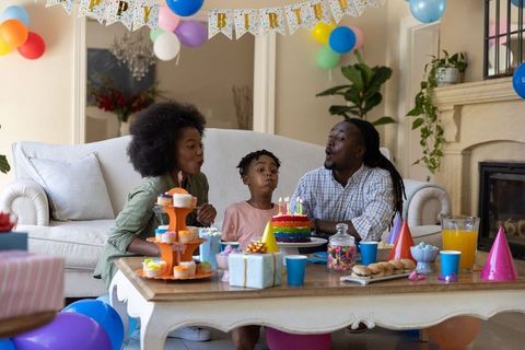 African american family blowing out birthday cake candles at home party with balloons