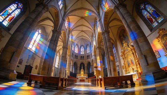 Sunlit gothic cathedral nave leading to gilded altar with stained glass reflections