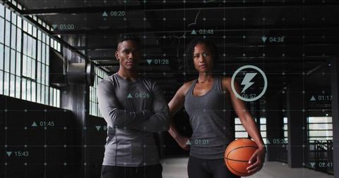 Standing athletic duo holding basketball in industrial gym with hud performance overlay