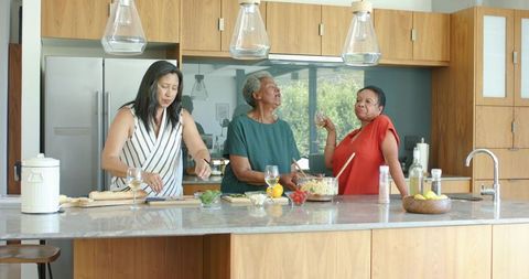Multigenerational women cooking together at modern kitchen island preparing salad