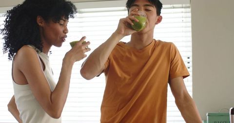 Mixed race couple drinking green smoothies in sunlit kitchen enjoying healthy morning