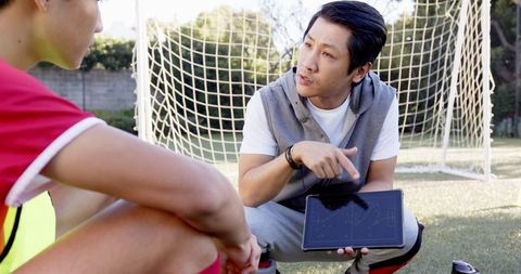 Soccer coach mentoring teen player with tablet strategy outside