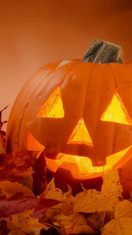 Vertical video zooming on glowing jack-o'-lantern with flickering light and autumn leaves