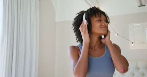 Relaxed woman adjusting headphones in cozy bedroom setting