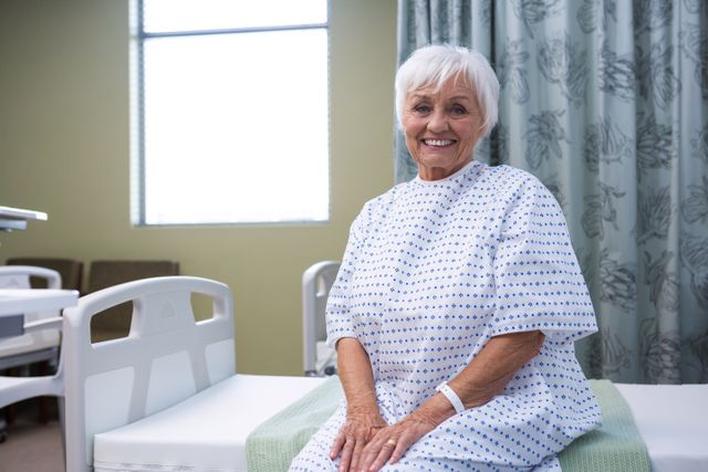 Elderly woman sitting on hospital bed, smiling and wearing a medical gown. Ideal for use in healthcare, medical, and wellness contexts, illustrating patient care, hospital stays, and recovery.