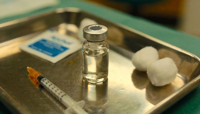 Preparing vaccine vial and syringe on sterile metal tray with cotton swabs and alcohol pad